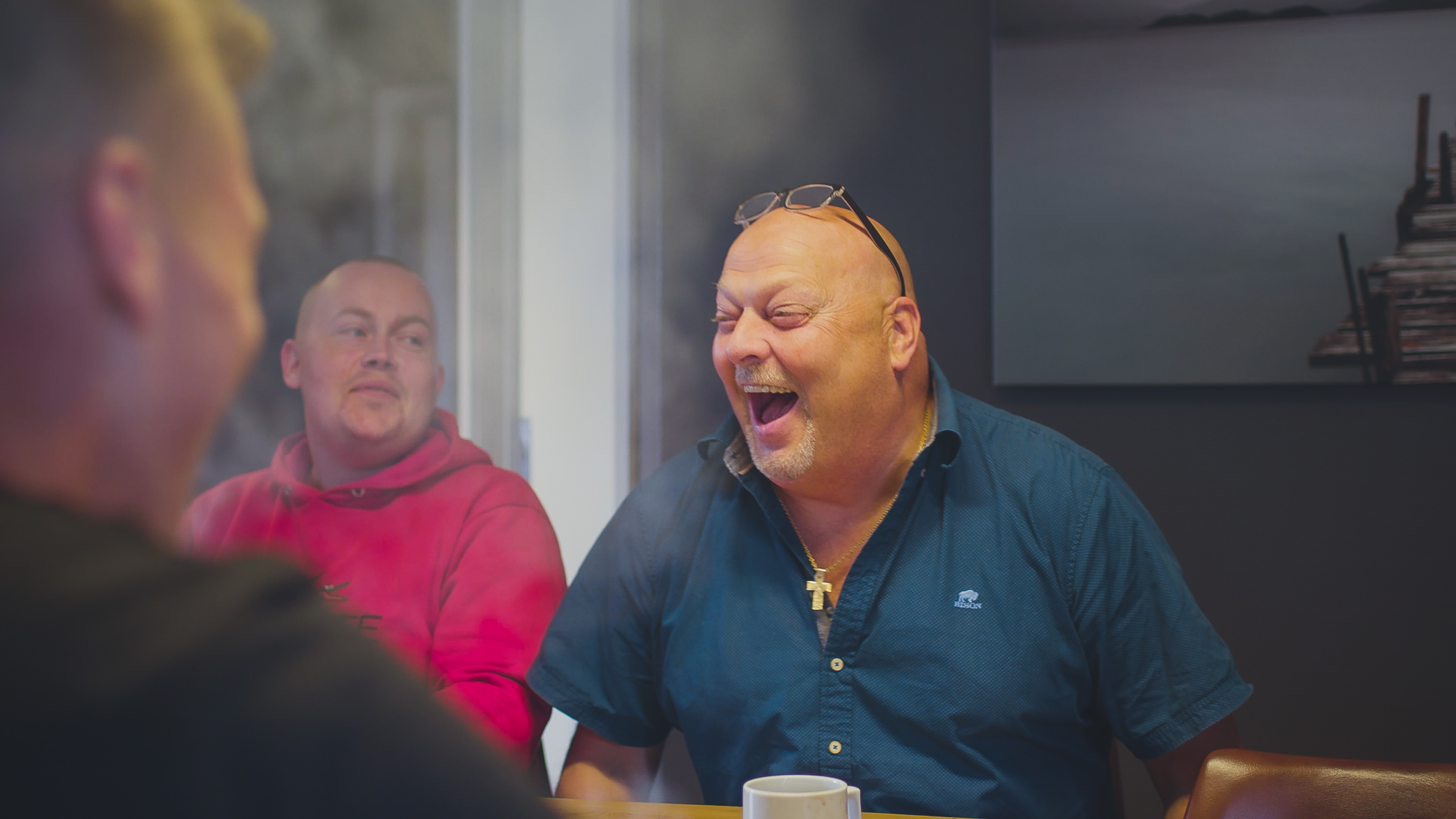 Personer samlet omkring et spisebord i munter samtale med grin og kaffekopper