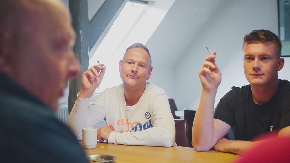 Mænd sidder samlet og taler sammen ved et bord i et lyst lokale