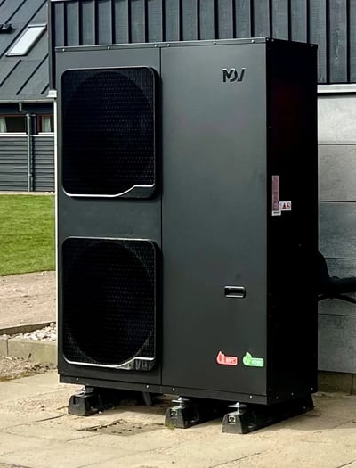 Installeret mørk varmepumpe-udedel med to store ventilatorfelter ved bygning