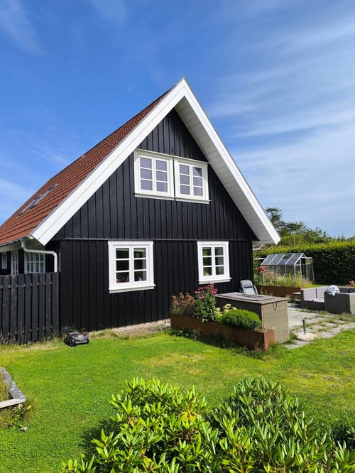 Sort træhus med rød tegltag og have