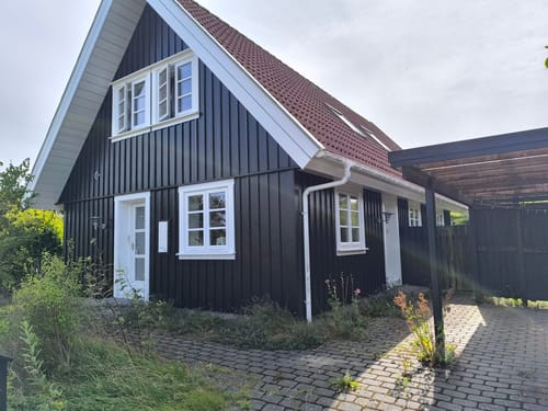 Sort træhus med rødt tegltag og carport