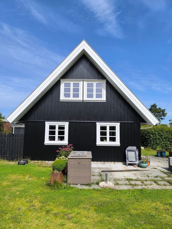 Sort træhus med hvid gavl under blå himmel