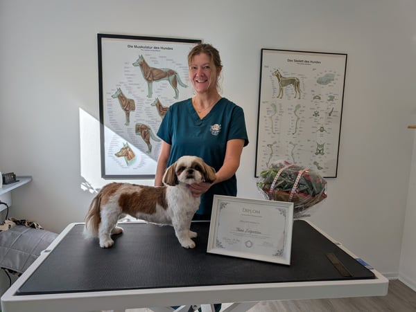 Uddannet hundefrisør Trine ved trimmebord med diplom og hund