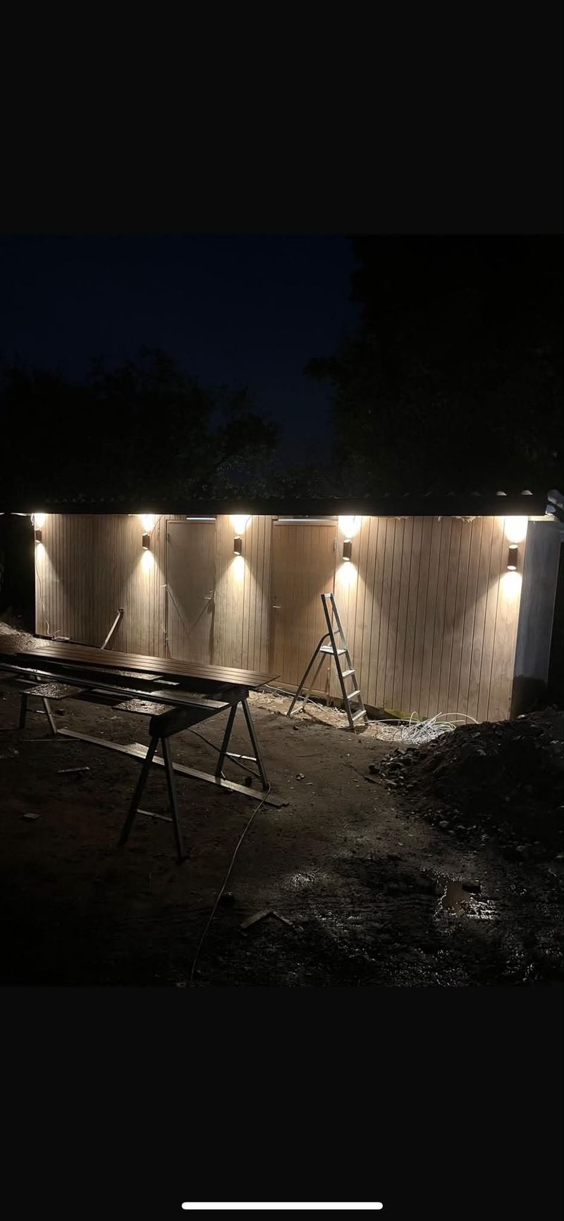 Flot aftenbelysning på nybygget facade – Udendørs bygning/facade fotograferet om aftenen, hvor flere udendørs væglamper er tændt og oplyser området.