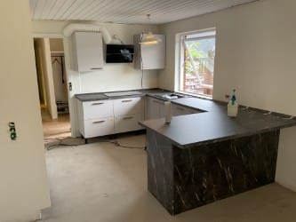 Køkkenmontering med hvide elementer og mørk bordplade – Køkken under renovering med hvide køkkenelementer og mørk bordplade. Gulv og dele af rummet er stadig under færdiggørelse.