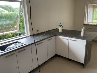 Køkkenmontering med vask og bordplade – Køkken under færdiggørelse med hvide underskabe, vask, bordplade og åbent vindue.