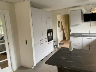Moderne hvidt køkken med højskabe og integrerede hvidevarer – Nyt eller renoveret køkken med hvide højskabe, integrerede hvidevarer og mørkt gulv.