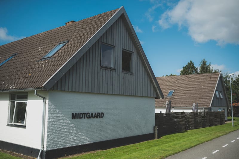Hvidmalet bygning med græsplæne og gavl i gråt træværk under blå himmel