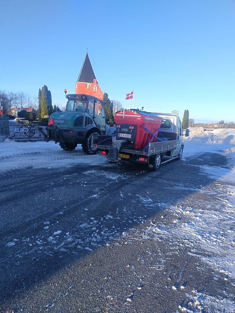 Ladvogn med saltspreder og traktor til snerydning foran landsbykirke